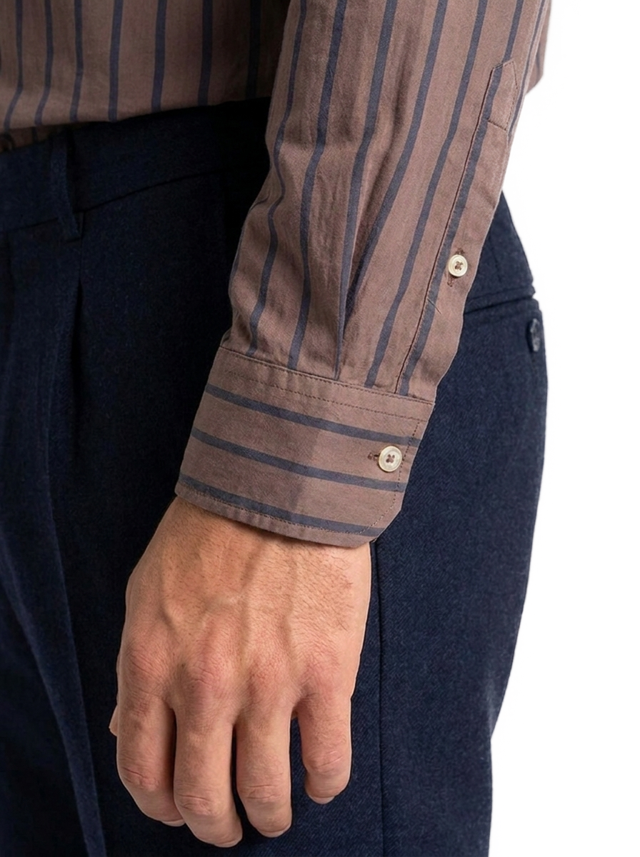 Dettaglio del polso della camicia uomo a righe marroni su fondo chiaro